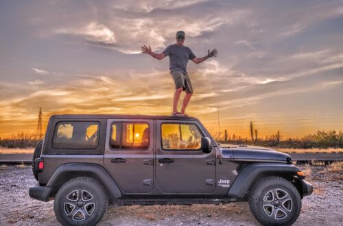 Paul is standing on top of a black Jeep Wrangler with a gorgeous sunset lighting up the sky behind him and through the Jeep's windows; Baja California Sur, Mexico