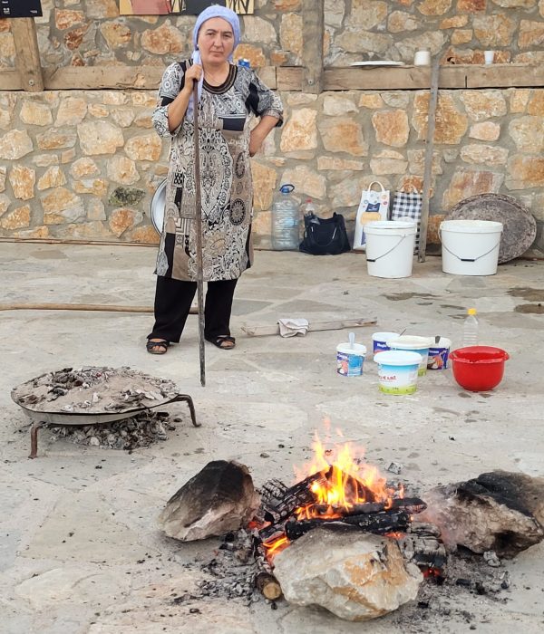 Kosovo woman standing by a firepit making flija @ Etno Fest; Kukaj, Kosovo