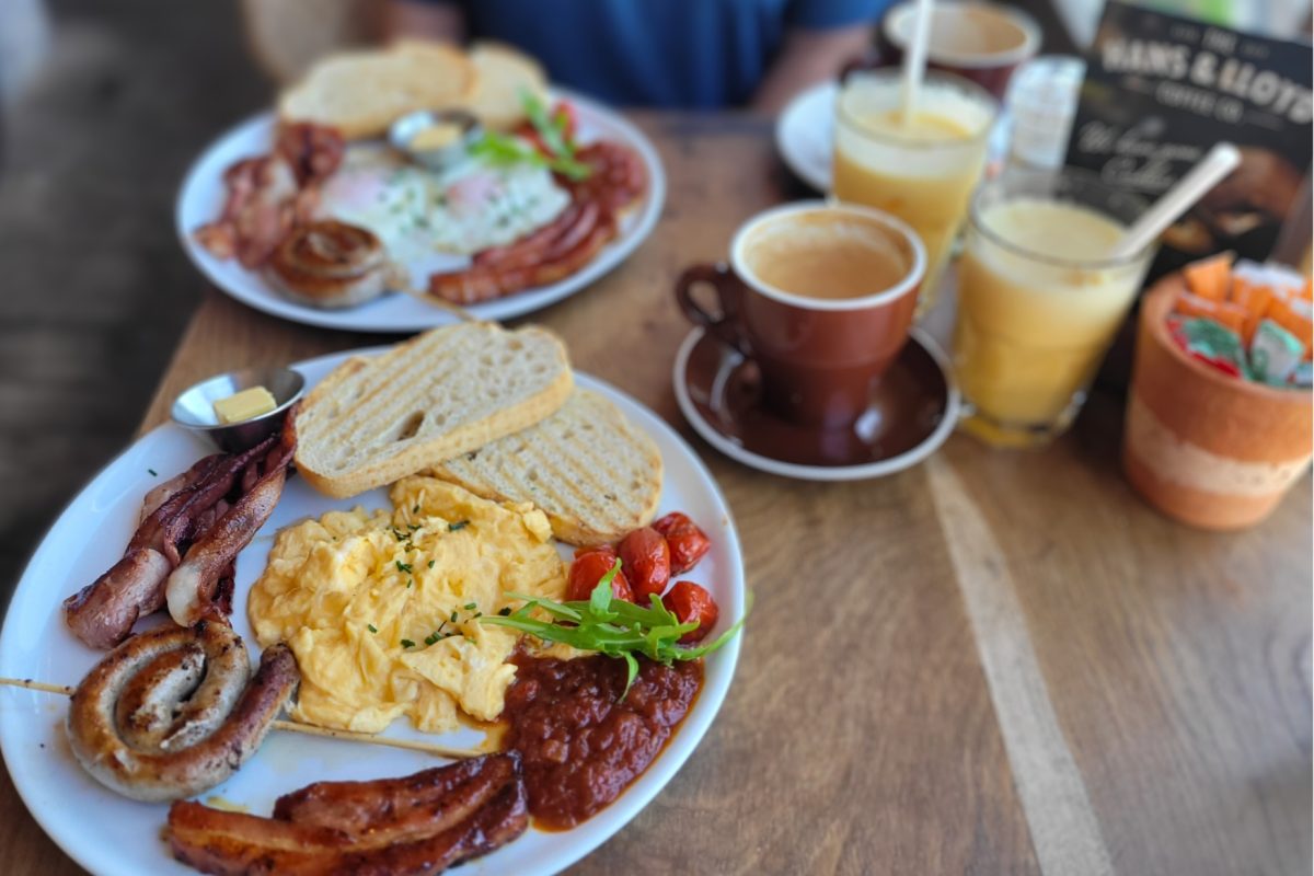 Full house breakfast with eggs, glazed pork, sausages, bacon, roasted baby tomatoes, and toast plus a cappuccino and a glass of orange juice @ Hans & Lloyd Coffee Co.; Muizenberg, South Africa